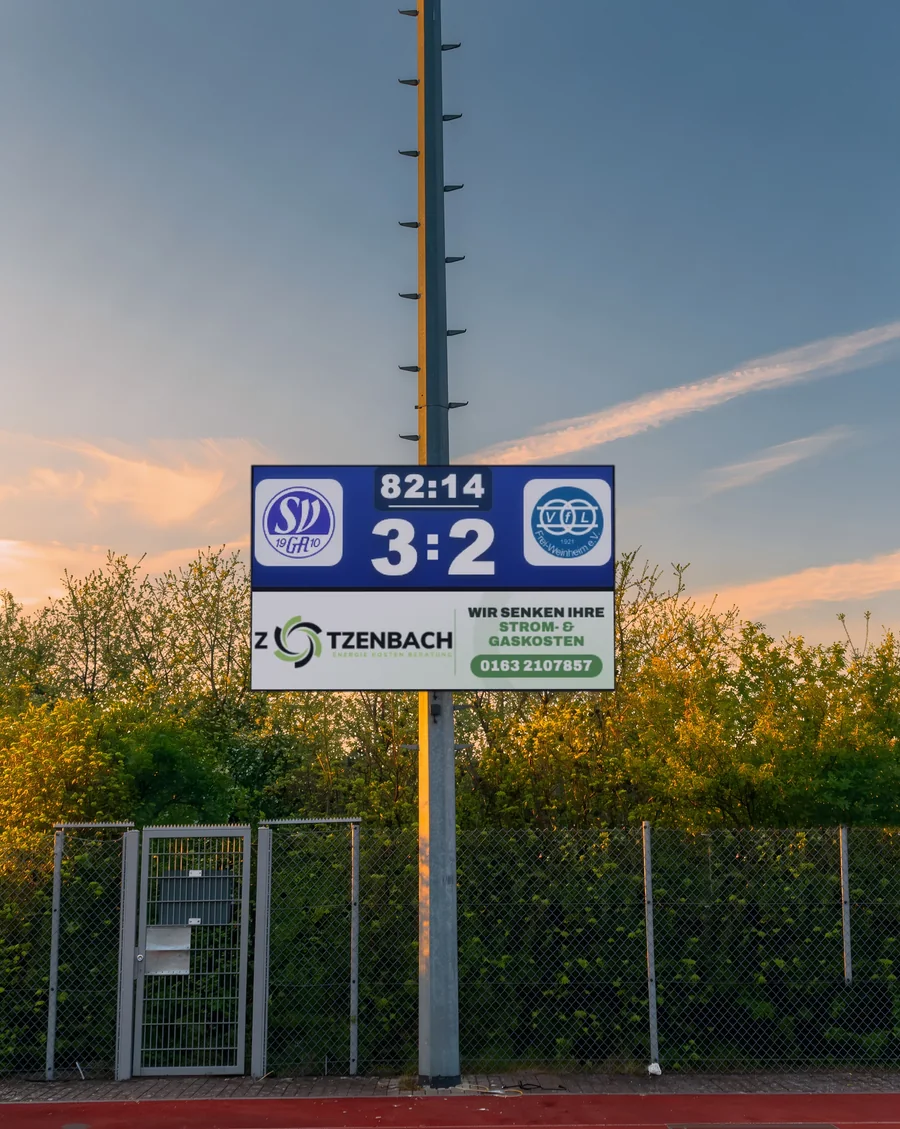 LED-Anzeigetafel am Mast im Abendrot, Spielstand 3:2 für den SV Gau-Algesheim, darunter Werbung eines Partners