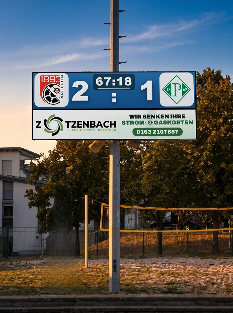 LED-Anzeigetafel am Fußballplatz in der Abendsonne mit Spielstand und Werbung eines regionalen Partners