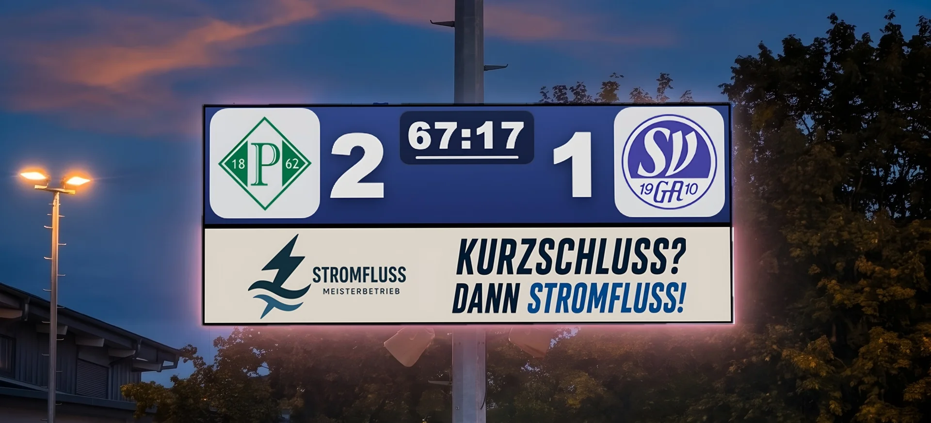 LED-Anzeigetafel leuchtet am Abend unter Flutlicht, Spielstand 2:1, darunter Werbung eines Partners